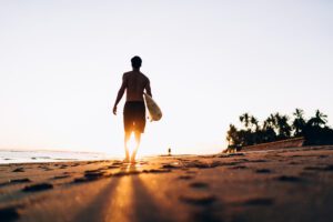 Rear view of sportive man walking at summer seashore with sunset spending day for practice hobby with surfboard, active male surfer enjoying travel vacations for catch wave in Dominicana Republic