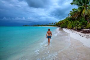 Back view teenage girl walking on a tropical beach with palm trees and ocean