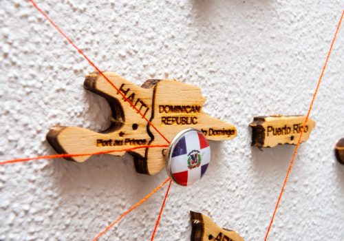 Dominican Republic flag on the pushpin with red thread showed the paths of movement or areas of influence in the global economy on the wooden map. Planning of traveling or logistic concept. Network connection.
